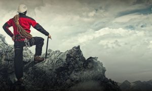 Rock climber on top of a mountain with a hero pose stance