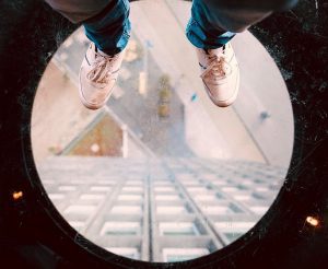 a glass floor with a pair of shoes in the frame looking down at a high-rise building.