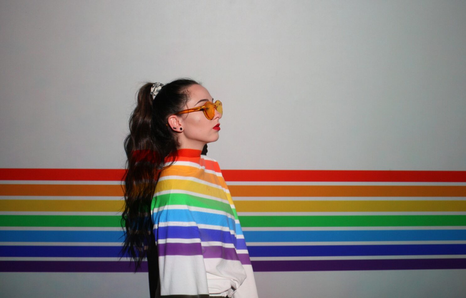 Women with a ponytail, sunglasses and a white hoddie with the random colors lines going across the image.