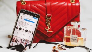 YSL red bag with an iPhone that has an Instagram page up, in front of the bag there is a Chanel perfume and some earings