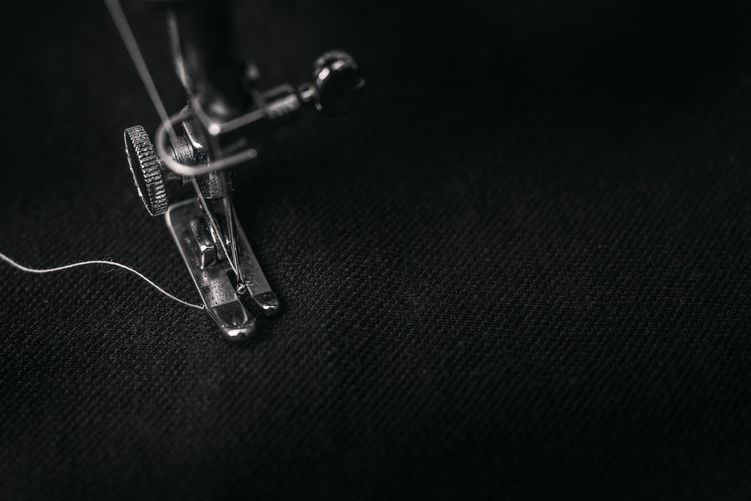 Black and white image of a sewing machine foot with fabric underneath. 