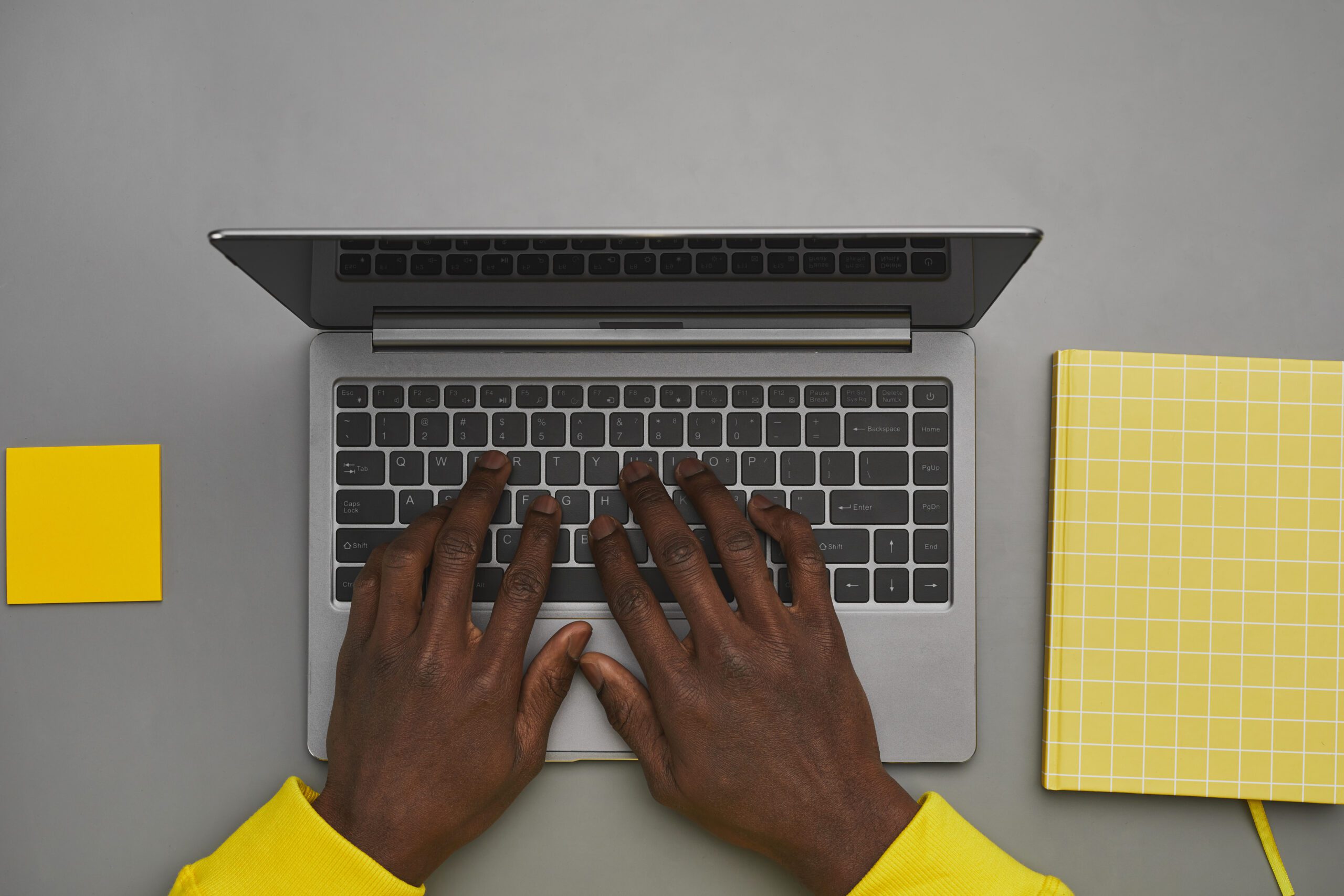 Graphic gray and yellow background of African-American male hands typing on laptop keyboard while working at desk, top down view, copy space