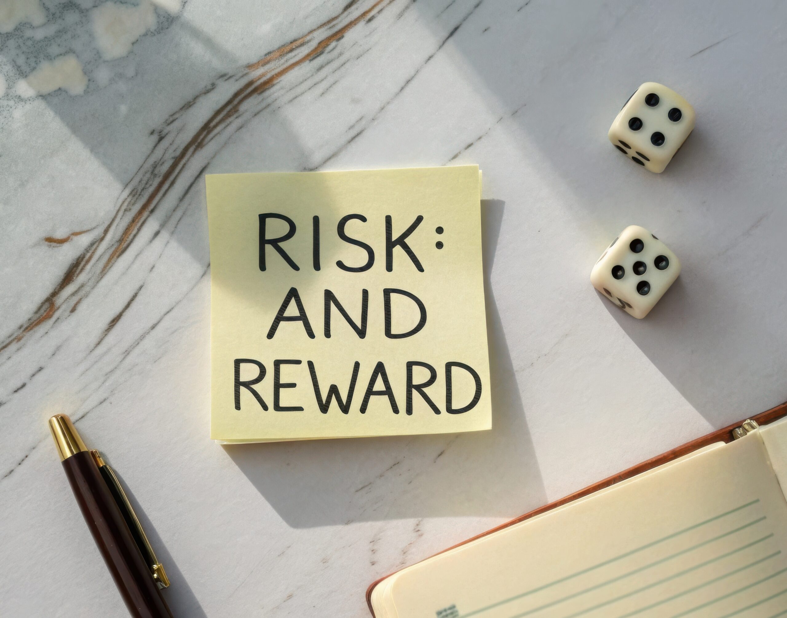 Creative concept of risk and reward displayed on sticky note with dice, pen, and journal on marble surface for business ideas
