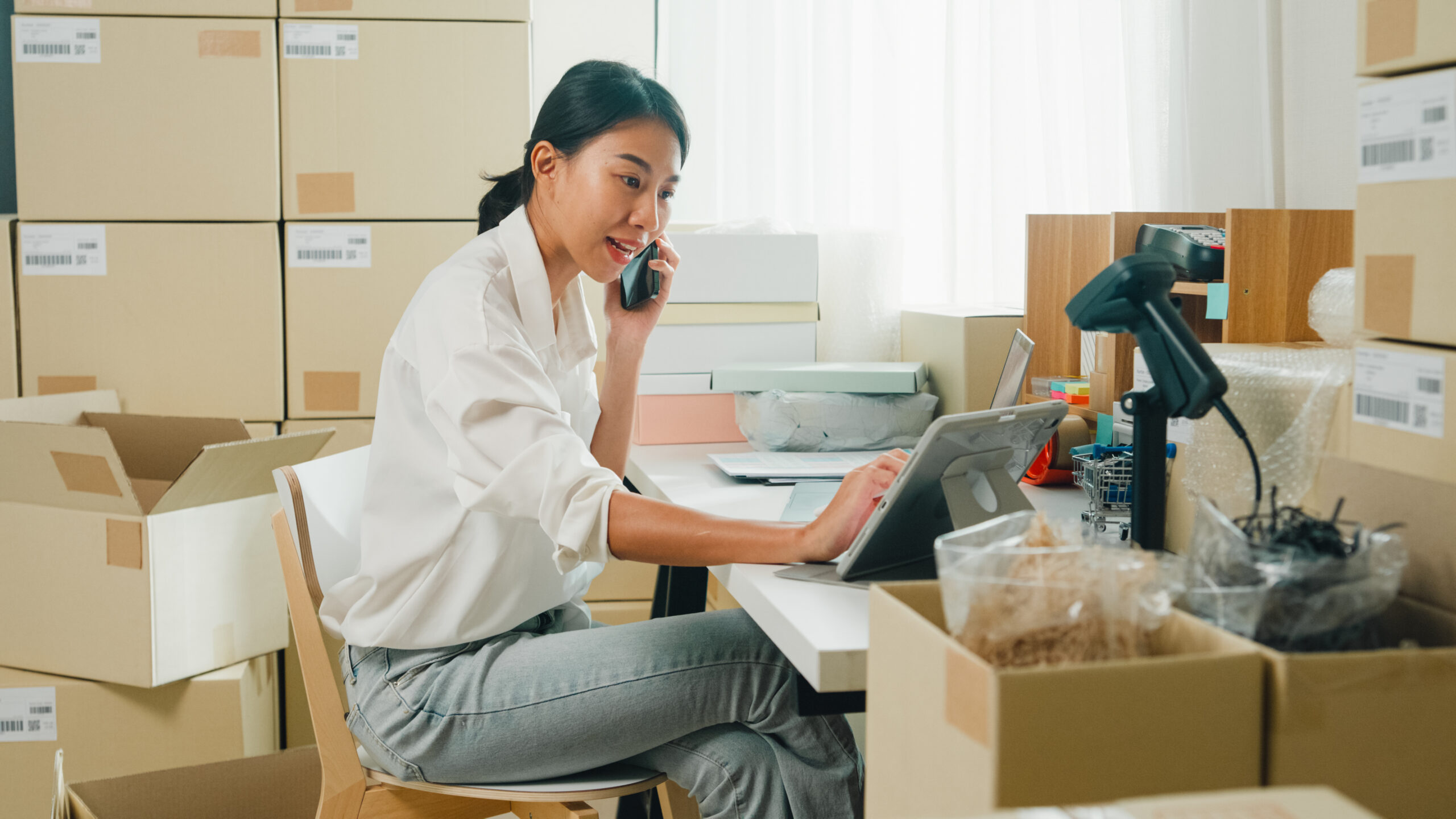 Youth attractive Asia female entrepreneur small business start up call smartphone confirm order with customer confirm check stock inventory product ready for delivery shipment at online retail shop.